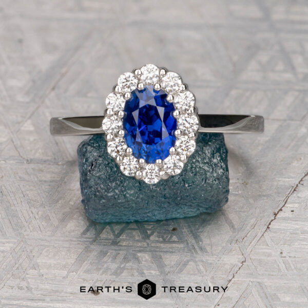 The "Elaine" ring in platinum with 1.44-carat Ceylon sapphire The "Elaine" ring in platinum, featuring a 1.44-carat Ceylon sapphire surrounded by accent stones, is displayed on a textured blue block with "Earth's Treasury" text below.