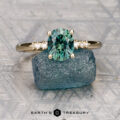 The "Paloma" ring in 14K yellow gold features a 1.67-carat Montana sapphire, displayed on a rough blue stone, with the "Earth's Treasury" logo shown below.