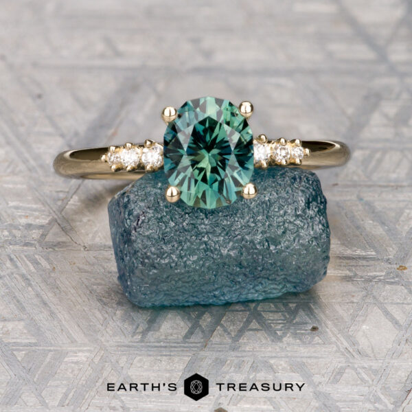 The "Paloma" ring in 14K yellow gold with 1.67-carat Montana sapphire The "Paloma" ring in 14K yellow gold features a 1.67-carat Montana sapphire, displayed on a rough blue stone, with the "Earth's Treasury" logo shown below.