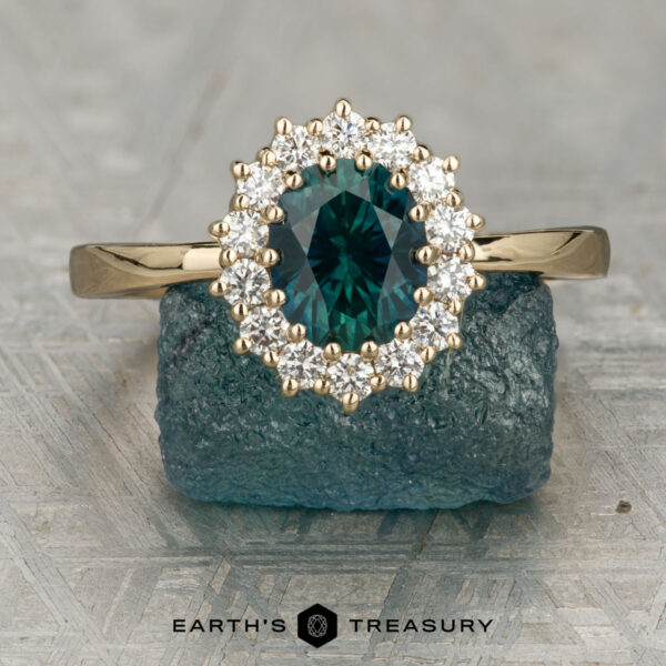 The "Vivian" ring in 14K yellow gold with 1.25-carat Montana sapphire The "Vivian" ring features a 1.25-carat Montana sapphire set in 14K yellow gold, accented by small diamonds and displayed on a rough blue crystal, with the "Earth's Treasury" logo below.