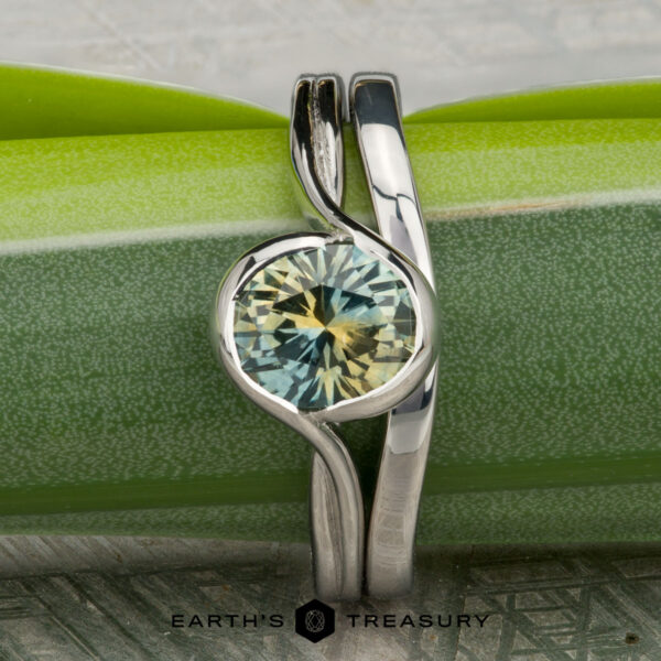 The "Milos" ring in platinum with 1.54-carat Montana sapphire, alongside the Custom-Fit Contour Band in platinum A 1.54-carat Montana sapphire "Milos" ring in platinum, paired with the Custom-Fit Contour Band in platinum, showcased against a green background.