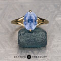 A Goel, Dhruv solitaire gold ring with a blue, oval gemstone featuring a starburst pattern is shown on a rough stone. The "Earth's Treasury" logo is displayed at the bottom.