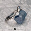 The "Multiflora" band in platinum, featuring three clear marquise stones and a blue pear-shaped stone, stands upright on a rough blue crystal with the "Earth's Treasury" logo below.