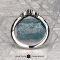 The "Multiflora" band in platinum, featuring three clear marquise stones and a blue pear-shaped stone, stands upright on a rough blue crystal with the "Earth's Treasury" logo below.