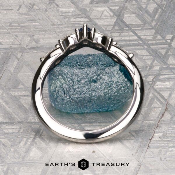 The "Multiflora" band in platinum The "Multiflora" band in platinum, featuring three clear marquise stones and a blue pear-shaped stone, stands upright on a rough blue crystal with the "Earth's Treasury" logo below.