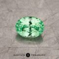A 4.43-carat light green Tsavorite garnet with an oval cut sits on a textured gray surface. The gem exhibits sparkling facets and reflections. Text at the bottom reads "Earth's Treasury".