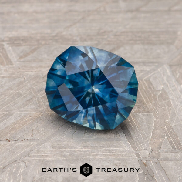 1.21-Carat Peacock Blue Montana Sapphire (Heated) A 1.21-carat Peacock Blue Montana Sapphire (heated) is shown on a textured gray surface, with "EARTH'S TREASURY" displayed at the bottom.