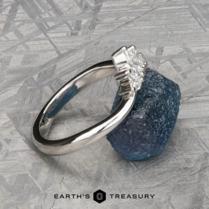 The "Vilaine" band in platinum is showcased atop a rough blue stone with a textured gray backdrop—ideal for any Vilaine Band fan looking to express their unique style.