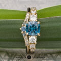 The Celosia ring in 14K yellow gold with a 1.43-carat Montana sapphire, shown with the Marseille band in 14K yellow gold, set against a green leafy background.