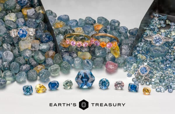 A collection of colorful gemstones, featuring the radiant Montana Sapphire from the Rock Creek Deposit, is displayed alongside two rings and a pair of earrings. The backdrop showcases rough stones, with a logo at the bottom that reads "Earth's Treasury.