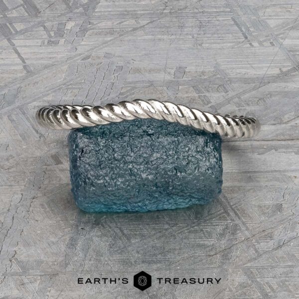 The "Winnie" band in platinum A platinum "Winnie" Band bracelet is displayed resting on a textured blue glass block, with the Earth's Treasury logo at the bottom of the image.