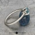 The "Winnie" ring showcases a platinum band adorned with a textured design and set with a 0.95-carat Montana sapphire. It sits elegantly on a rough blue stone against a gray background, capturing the sophistication of "Earth's Treasury.