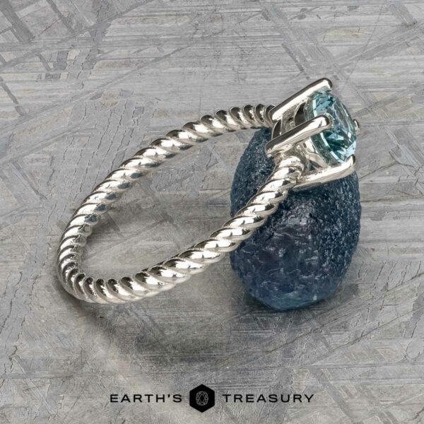 The "Winnie" ring in platinum with 0.95-carat Montana sapphire The "Winnie" ring showcases a platinum band adorned with a textured design and set with a 0.95-carat Montana sapphire. It sits elegantly on a rough blue stone against a gray background, capturing the sophistication of "Earth's Treasury.