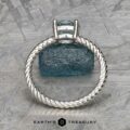 The "Winnie" ring, crafted in platinum with a 0.95-carat Montana sapphire, elegantly displayed on a textured blue-green surface like the soothing notes of music.