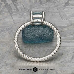 The "Winnie" ring, crafted in platinum with a 0.95-carat Montana sapphire, elegantly displayed on a textured blue-green surface like the soothing notes of music.