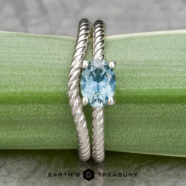 The "Winnie" ring in platinum with 0.95-carat Montana sapphire, alongside the "Winnie" band in platinum A twisting platinum band adorned with a 0.95-carat Montana sapphire is elegantly displayed on a green leaf, reminiscent of something the "Winnie" ring might cherish.