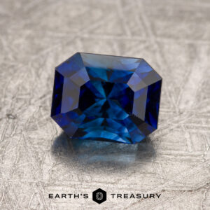 A deep blue, faceted 1.78-Carat Ceylon Sapphire with an octagonal shape rests on a textured metallic surface. The words "EARTH'S TREASURY" appear below.