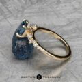 The "Catarina" ring in 14k yellow gold showcases a breathtaking 1.64-carat Montana sapphire at its center, adorned with dazzling diamonds. It is elegantly presented against a raw blue gemstone backdrop on a textured gray surface, radiating timeless sophistication.