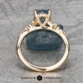 Set against a textured gray background, The "Catarina" ring in 14k yellow gold showcases a 1.64-carat Montana sapphire, elegantly surrounded by small radiant diamonds.