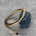 The "Catarina" band in 14k yellow gold, adorned with diamonds, elegantly rests against a rough blue stone on a textured gray surface.