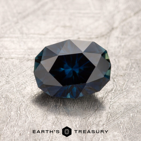 1.27-Carat Australian Sapphire A 1.27-carat Australian Sapphire, faceted in Midnight Blue, rests on a textured, light-colored surface with the "EARTH'S TREASURY" logo and text beneath it.