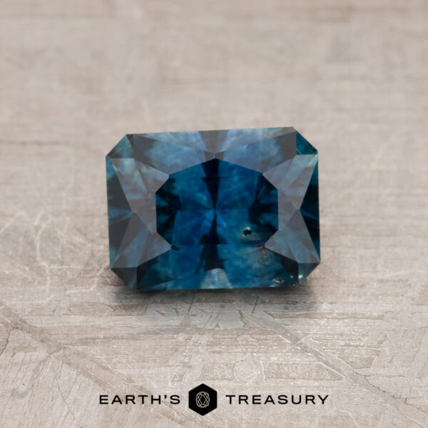 0.98-Carat Montana Sapphire (Heated) A 0.98-carat heated Montana Sapphire gemstone is placed on a textured surface with the "EARTH'S TREASURY" logo and text below it.