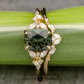 Introducing "The Holly Band," a stunning green gemstone ring featuring a dark green central stone encircled by small diamonds, all set in a radiant gold band. The ring is elegantly displayed on a green and white background, with the text "Earth's Treasury" at the bottom.