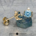 Gold earrings adorned with aquamarine gemstones and a heated cushion-cut green-blue stone are elegantly showcased on a textured surface, echoing the style of the EA-MS-432 earrings.