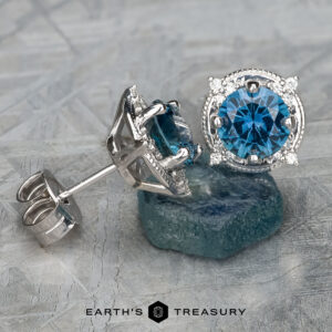 A pair of EA-MS-509 silver halo earrings adorned with large Montana Sapphire gemstones, elegantly displayed on a textured surface.