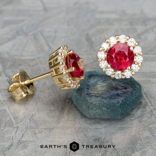 EA-DB-504 The EA-DB-504 earrings, featuring 5.0mm heated red stones surrounded by sparkling diamonds, are elegantly displayed on a textured surface.