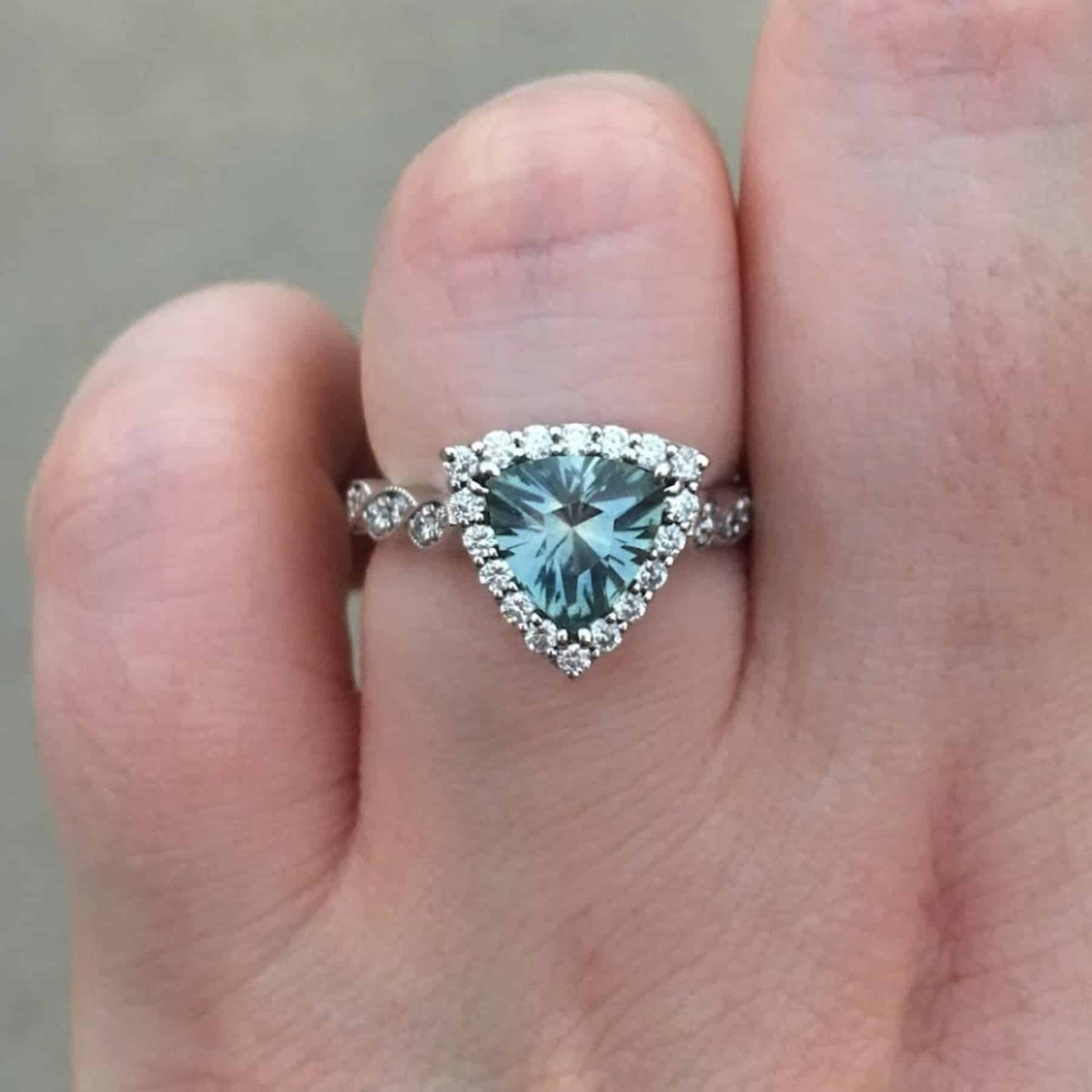 A photo from a customer review featuring a custom halo ring with twisted diamond-accented band and a large aqua trillion Montana sapphire