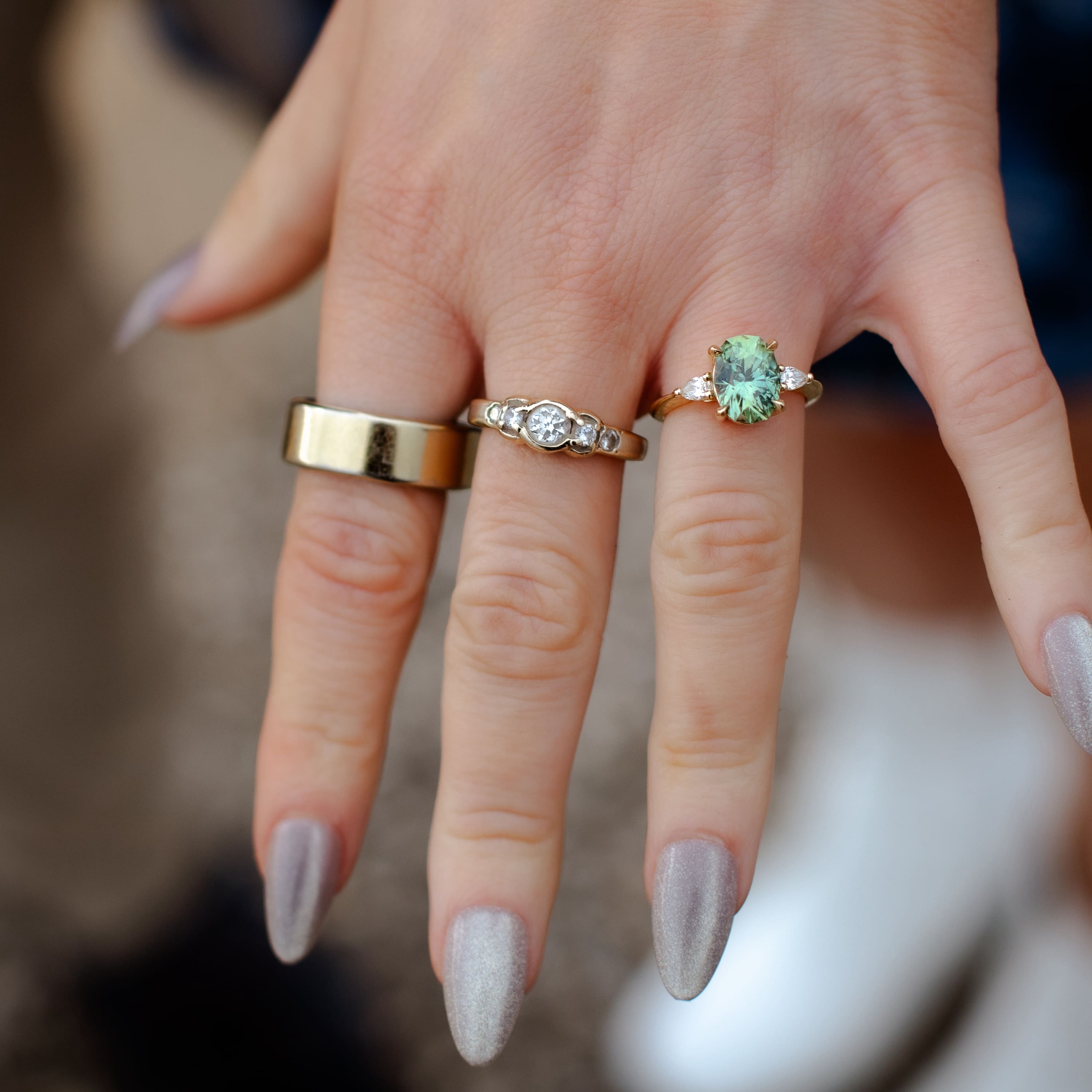 A photo from a customer review with two rings not made by Earth's treasury, then on the right: a custom three stone ring in 14k yellow gold with a 3.50-Carat Montana Sapphire