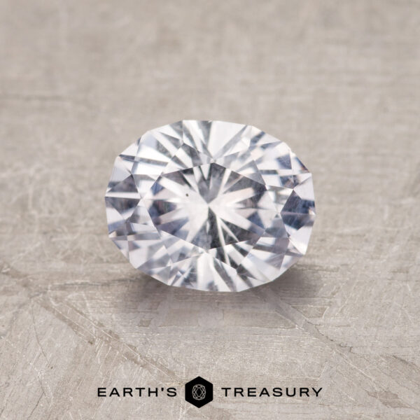 1.19-Carat Near Colorless Montana Sapphire The 1.19-Carat Near Colorless Montana Sapphire, faceted in a brilliant oval cut, is displayed on a textured surface with "EARTH'S TREASURY" at the bottom.