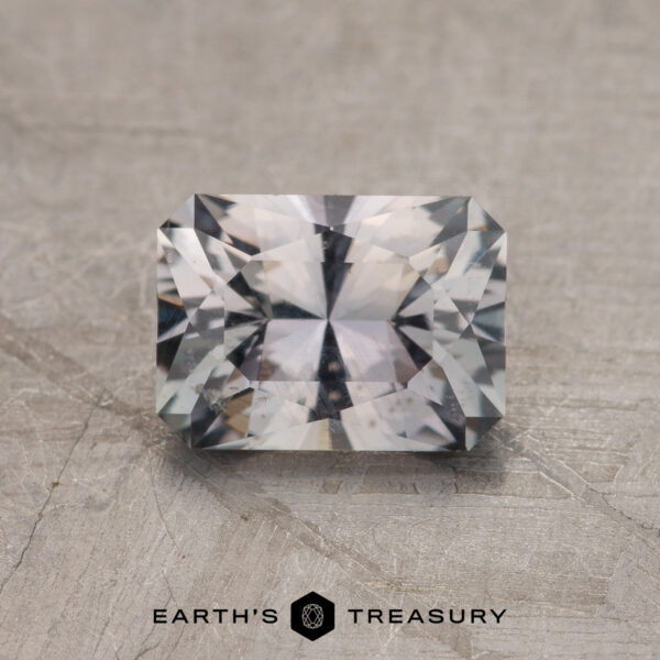 1.29-Carat Gray Montana Sapphire A 1.29-carat rectangular faceted Gray Montana Sapphire with a complex cut rests on a textured surface, featuring the "EARTH'S TREASURY" text at the bottom.