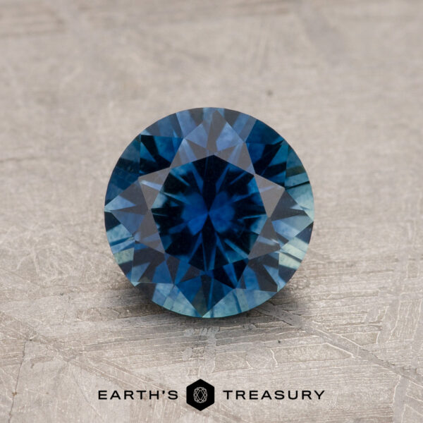 1.19-Carat Rich Blue Montana Sapphire (Heated) A 1.19-carat rich blue heated Montana Sapphire is displayed on a textured surface, with the "Earth's Treasury" logo and text beneath it.