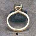 The "Kerria" Solitaire ring, set with a light green gemstone in an elegant V-shaped prong setting, features a sleek, modern design. Displayed upright on a textured gray surface, it is accompanied by the brand name "Earth's Treasury" below.