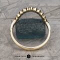 The "Taurion" Band, a gold ring featuring a unique scalloped edge design, is displayed upright on a flat surface with an uneven, dark blue textured rock in the center. The background has a geometric pattern, and the text "EARTH'S TREASURY" is visible at the bottom of the image.