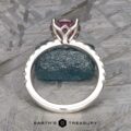 The Classic Pave "Blumia" Ring features a stunning large pink gemstone set in a silver band, which is adorned with small, sparkling diamonds. It is displayed upright against a textured background, with the text "Earth's Treasury" visible at the bottom center.