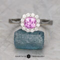 The Rosenthal, Aaron ring features a round pink gemstone prong-set, surrounded by small diamonds in silver, displayed on rough blue crystal. Set against a light gray background with "EARTH'S TREASURY" text below.