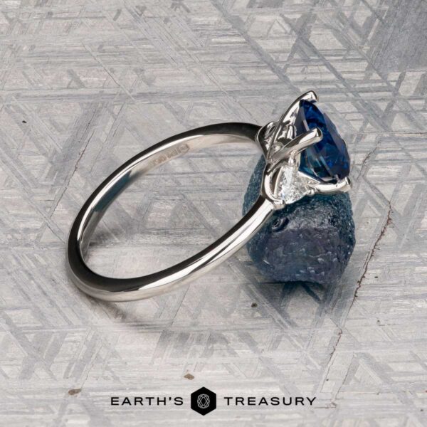 The "Vesta" ring in platinum with 2.44-carat Montana sapphire The "Vesta" ring in platinum, set with a 2.44-carat Montana sapphire, is shown on a rough blue stone against a geometric metallic background featuring the "EARTH'S TREASURY" logo at the bottom.