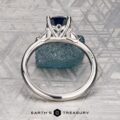 The "Vesta" ring in platinum, set with a 2.44-carat Montana sapphire, is shown on a rough blue stone against a geometric metallic background featuring the "EARTH'S TREASURY" logo at the bottom.