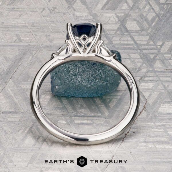 The "Vesta" ring in platinum with 2.44-carat Montana sapphire The "Vesta" ring in platinum, set with a 2.44-carat Montana sapphire, is shown on a rough blue stone against a geometric metallic background featuring the "EARTH'S TREASURY" logo at the bottom.