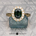 The Pave "Valeria" ring in 18K yellow gold showcases a 1.59-carat Australian sapphire encircled by pavé diamonds, displayed on a rough blue stone with a geometric-patterned backdrop.