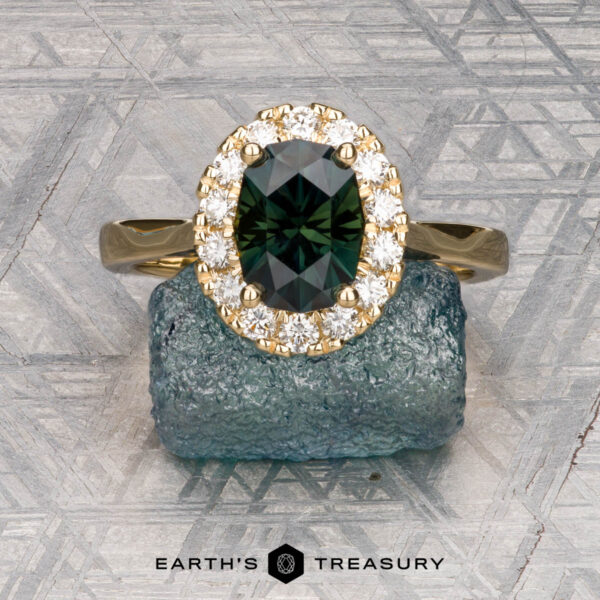 The Pave "Valeria" ring in 18K yellow gold with 1.59-carat Australian sapphire The Pave "Valeria" ring in 18K yellow gold showcases a 1.59-carat Australian sapphire encircled by pavé diamonds, displayed on a rough blue stone with a geometric-patterned backdrop.