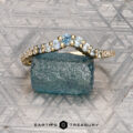 The "Venus" band in 18K yellow gold, featuring a row of white gemstones, is displayed on a rough blue-green stone atop a patterned gray surface, with the "Earth's Treasury" logo at the bottom.