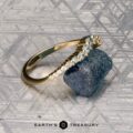 The "Venus" band in 18K yellow gold, featuring a row of white gemstones, is displayed on a rough blue-green stone atop a patterned gray surface, with the "Earth's Treasury" logo at the bottom.
