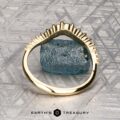 The "Venus" band in 18K yellow gold, featuring a row of white gemstones, is displayed on a rough blue-green stone atop a patterned gray surface, with the "Earth's Treasury" logo at the bottom.