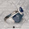 The Pave "Valeria" ring in platinum features a 1.41-carat Ceylon sapphire and pave-set diamonds, shown on a rough blue stone with engraved patterns in the background.