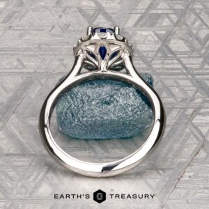 The Pave "Valeria" ring in platinum features a 1.41-carat Ceylon sapphire and pave-set diamonds, shown on a rough blue stone with engraved patterns in the background.