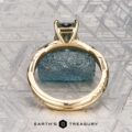 The "Waltz" ring in 18K yellow gold, featuring a 1.67-carat rectangular Montana sapphire and diamond accents, is displayed on a rough blue stone with the "Earth's Treasury" logo beneath.
